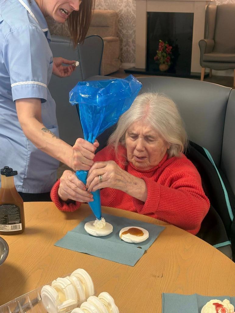 carer helping an older lady with a piping bag