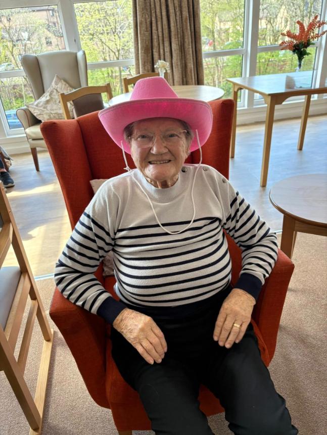 older lady sat down in an armchair wearing a pink cowboy hat