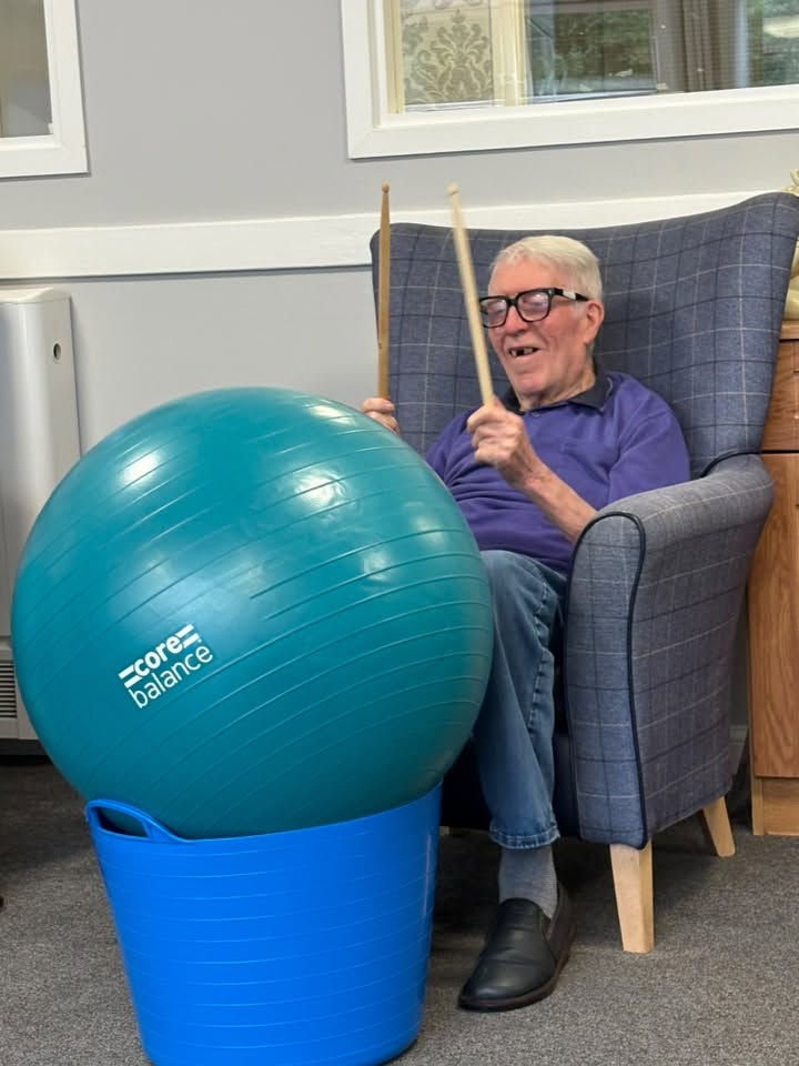elderly man hitting exercise ball with drum sticks in care home activity