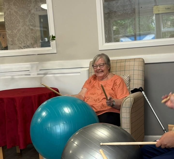elderly man hitting exercise ball with drum sticks in care home activity