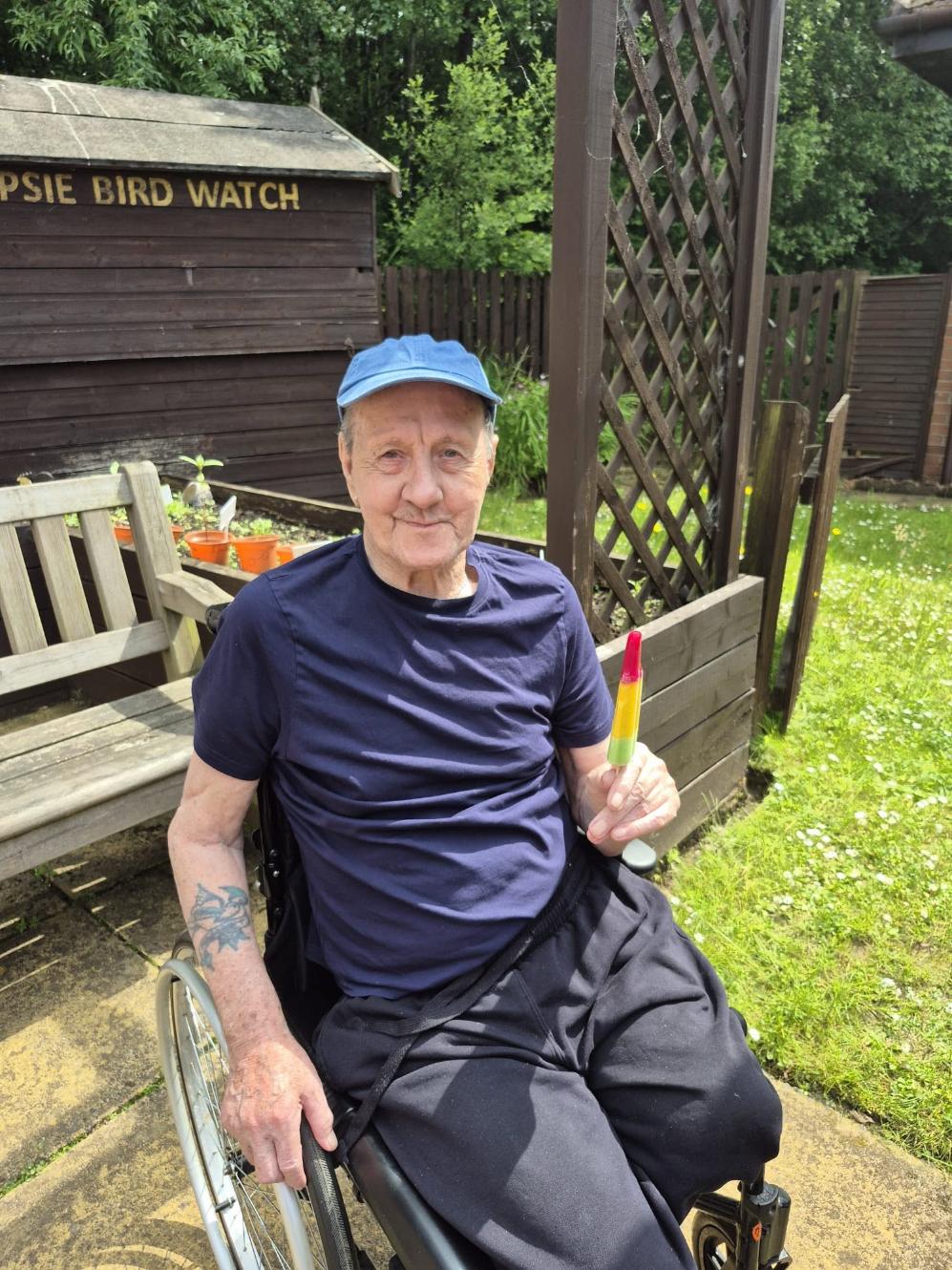 elderly man in wheelchair sat outside with an ice lolly