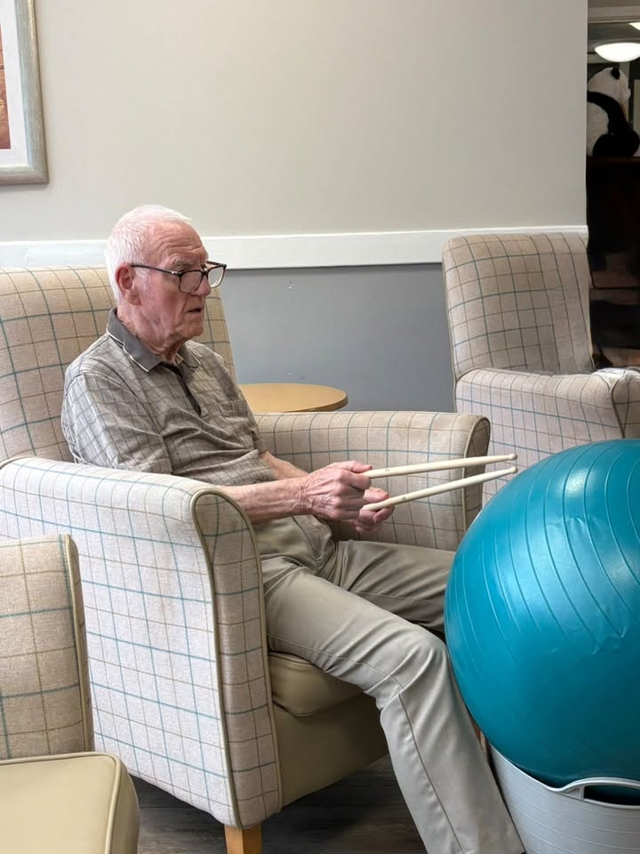elderly man hitting exercise ball with drum sticks in care home activity